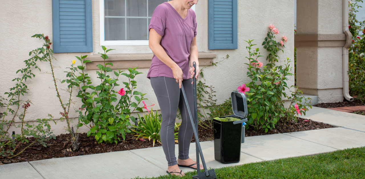 Woman cleaning up pet waste with a scooper in her front yard, emphasizing pet cleanup and responsible ownership