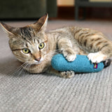 A tabby cat with striking green eyes playfully engages with its new favorite toy, the Mad Cat Wacky Wool Crinkle Kicker, a natural wool plush sprinkled with catnip silvervine, on a carpeted floor.