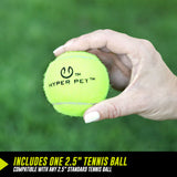 A white-polished hand holds a bright yellow-green tennis ball labeled Hyper Pet over grass, ideal for playtime. It includes one 2.5 ball, compatible with any standard 2.5 ball and the Hyperpet K9 Kannon Pro Ball Launcher by Hyperpet.