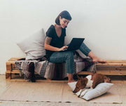 Woman typing on a laptop while her dog sleeps on a pillow