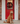 A red Golden Doodle stands on the front porch of a brick house with a red door featuring a Christmas wreath.