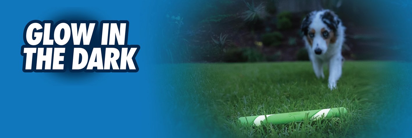 A dog runs towards a glowing green stick on grass, surrounded by a blue background. Bold white text on the left reads Glow in the Dark.