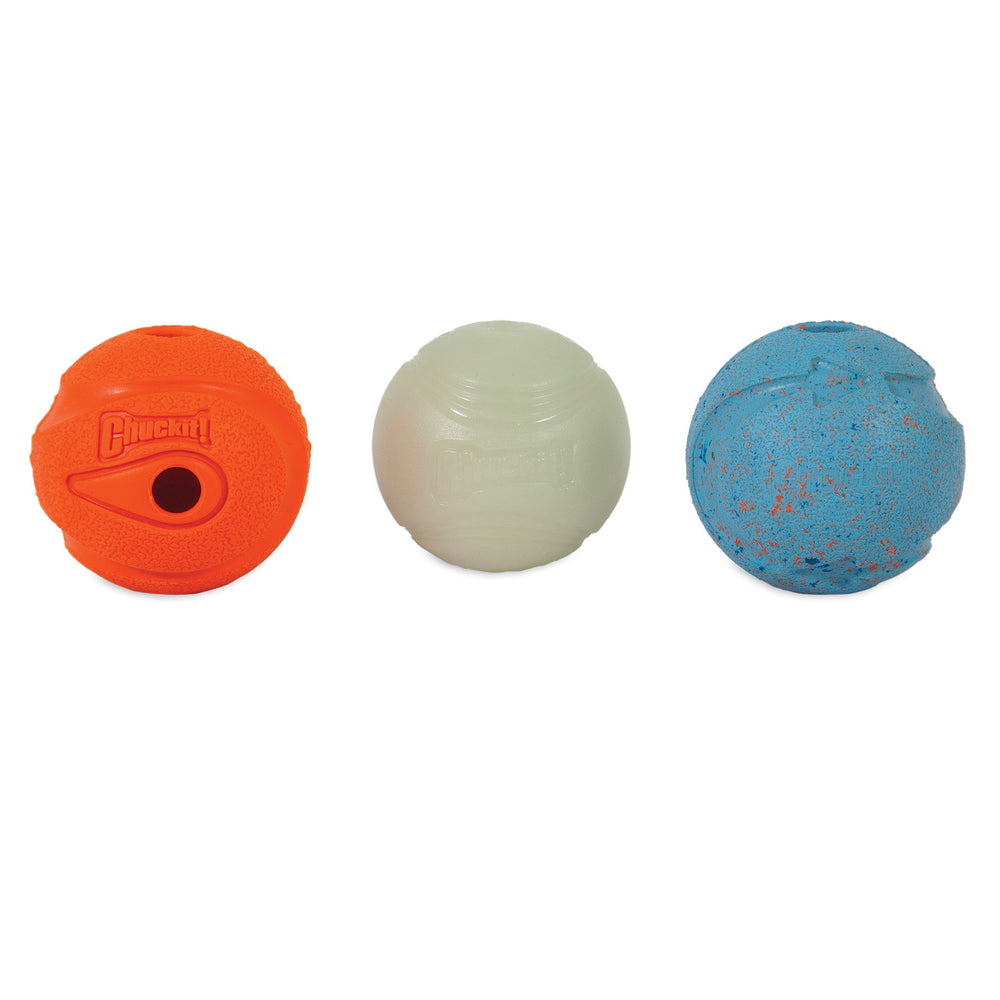 Three textured dog balls are aligned horizontally: The left one is an orange Chuckit! Whistler with a hole, the middle is a white smooth Max Glow Ball, and the right one is blue with orange speckles. Each ball in the Chuckit! Medium Fetch Medley Dog Ball Set proudly displays the Chuckit brand logo.
