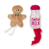 A plush gingerbread man toy with googly eyes, a bow tie, and wavy arms sits beside Mad Cat Santa Claws Milk. The milk bottle has a pink cap and a playful red feather at the bottom.