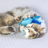 A fluffy calico cat lies on a white textured surface, playfully snuggling the Quirky Kitty Octopurr Kicker – an ocean-themed catnip kicker toy with ribbon accents from Quirky Kitty.