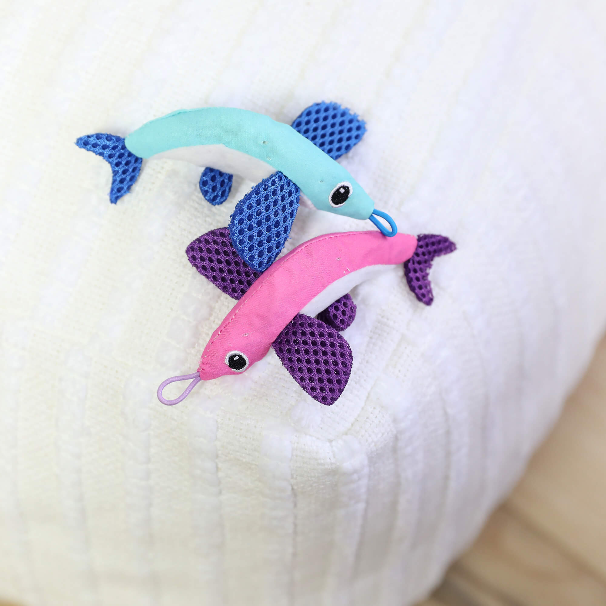 The Quirky Kitty Flying Fish 2pk—Interactive Catnip Cat Toys with Slingshot—features a blue and a pink fish, each with purple fins, large stitched eyes, and looped mouths on a white textured surface.