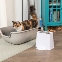 A calico cat sits in a beige litter box on a textured mat, while a ginger cat peeks from behind a turquoise bookshelf filled with books. Nearby, the PetFusion 2-in-1 Universal Litter Scoop Holder is conveniently placed. The waterproof hypoallergenic silicone mat ensures durability and easy maintenance.