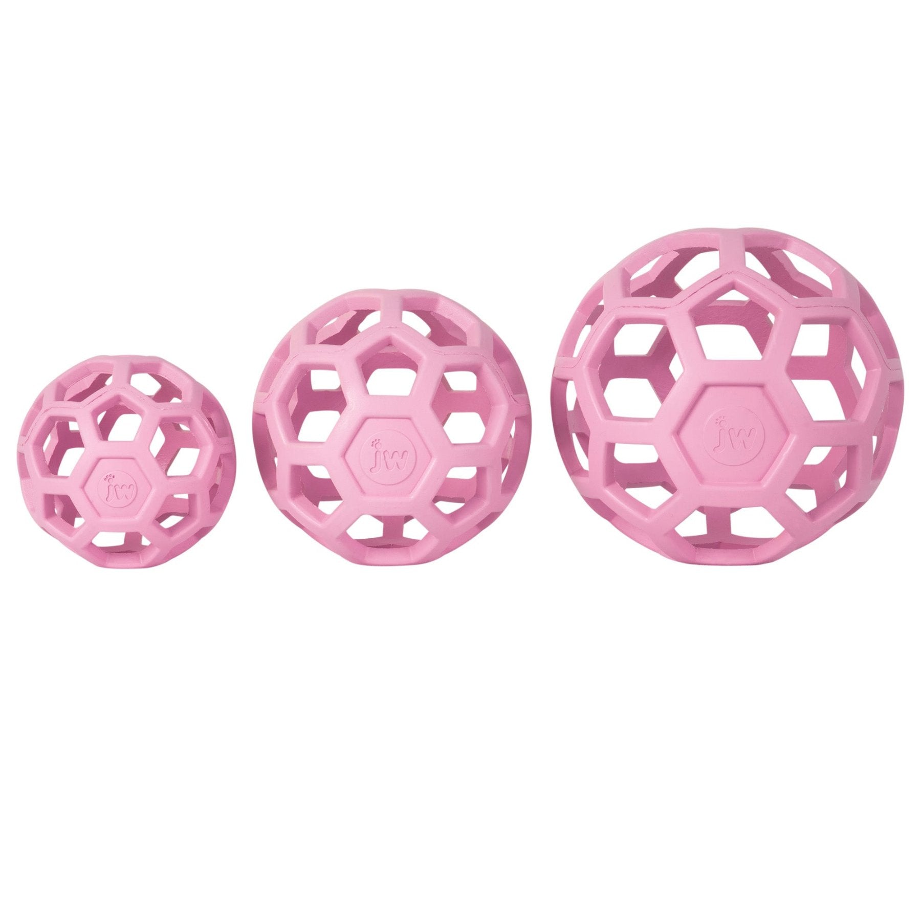 Three pink JW Hol-EE Roller Trend-EE puzzle balls of varying sizes, made from natural rubber with a hexagonal lattice design, are lined up in ascending order from left to right. Each ball provides mental stimulation for dogs and features JW embossed on a panel.