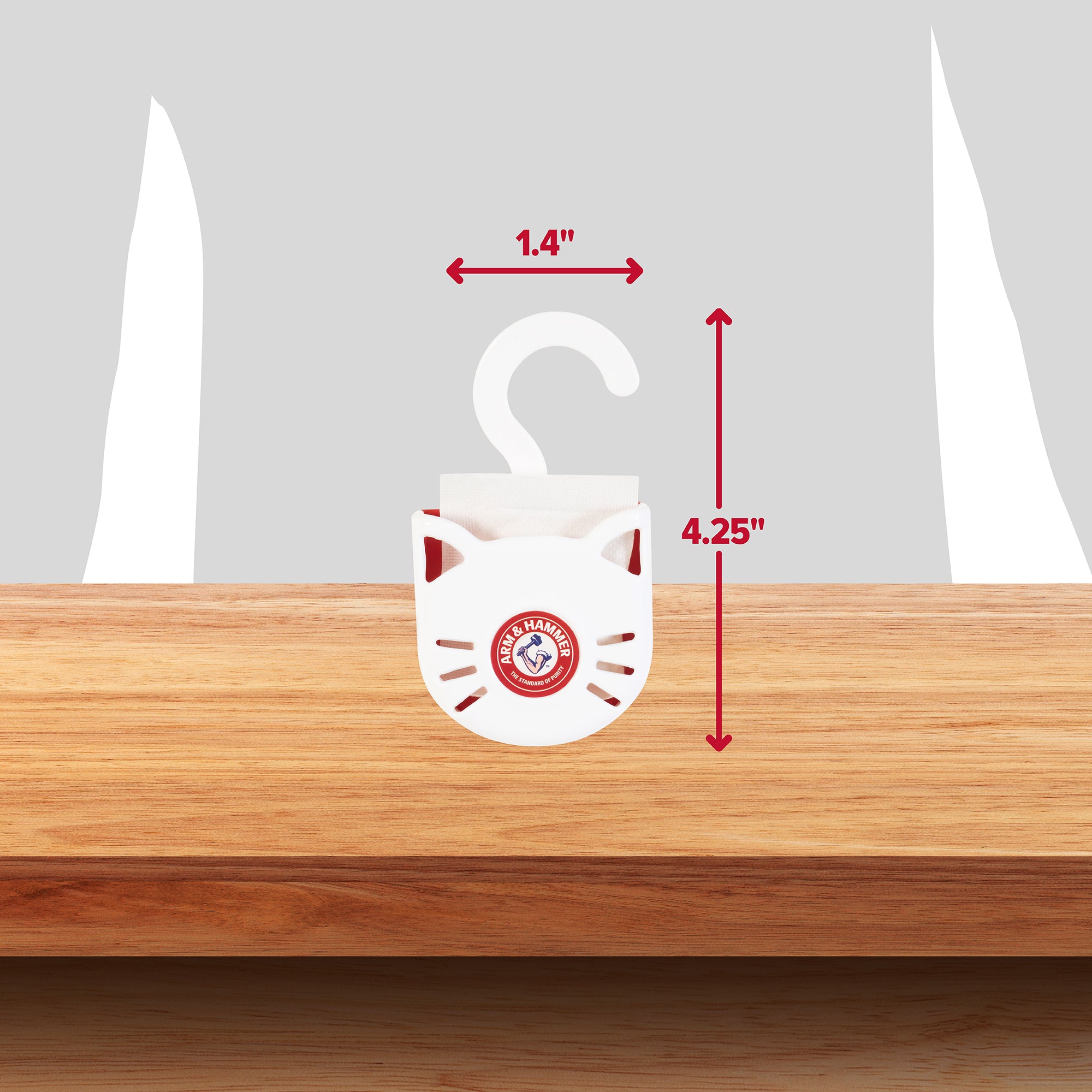 The Arm & Hammer Purifying Pak Cat Litter Deodorizer, featuring a white cat shape with a red logo, hangs on wood. Sized 1.4 inches wide and 4.25 inches tall, it neutralizes litter box odors for a fresh environment against a gray backdrop.