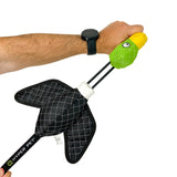 In a persons hand is the green and yellow Hyperpet Flying Duck Launching Dog Toy, featuring quilted black wings on a stick with a black grip. The individual, wearing a black watch, is ready to launch the slingshot toy for their dogs entertainment.
