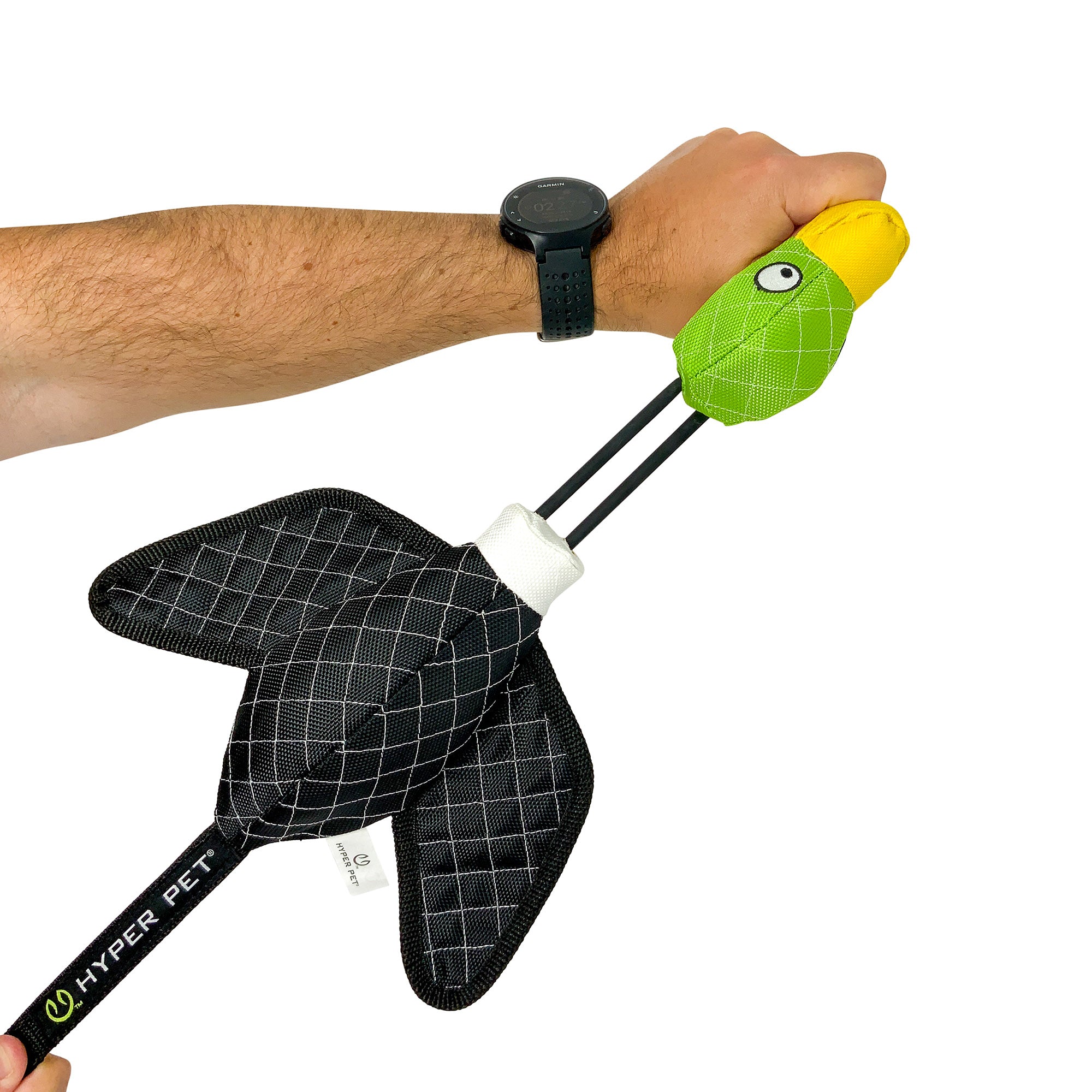 In a persons hand is the green and yellow Hyperpet Flying Duck Launching Dog Toy, featuring quilted black wings on a stick with a black grip. The individual, wearing a black watch, is ready to launch the slingshot toy for their dogs entertainment.