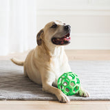 A tan dog lies on a gray rug, grinning cheerfully with its paws on a versatile JW Hol-ee Roller Dog Toy by Jw, made from natural rubber. A softly lit background creates a warm and cozy atmosphere.