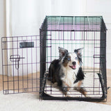 A medium dog with black, white, and gray fur lounges on the SnooZZy Natural Quilted Kennel Mat made of machine washable super-soft fabric. The open black metal crate is in a bright room with white walls, providing comfort and durability.