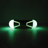 The Chuckit! Tumble Bumper Max Glow by Chuckit illuminates two ends with a black core in a dark environment. Its cylindrical shape and glowing green light resemble a futuristic fetch toy from another world.