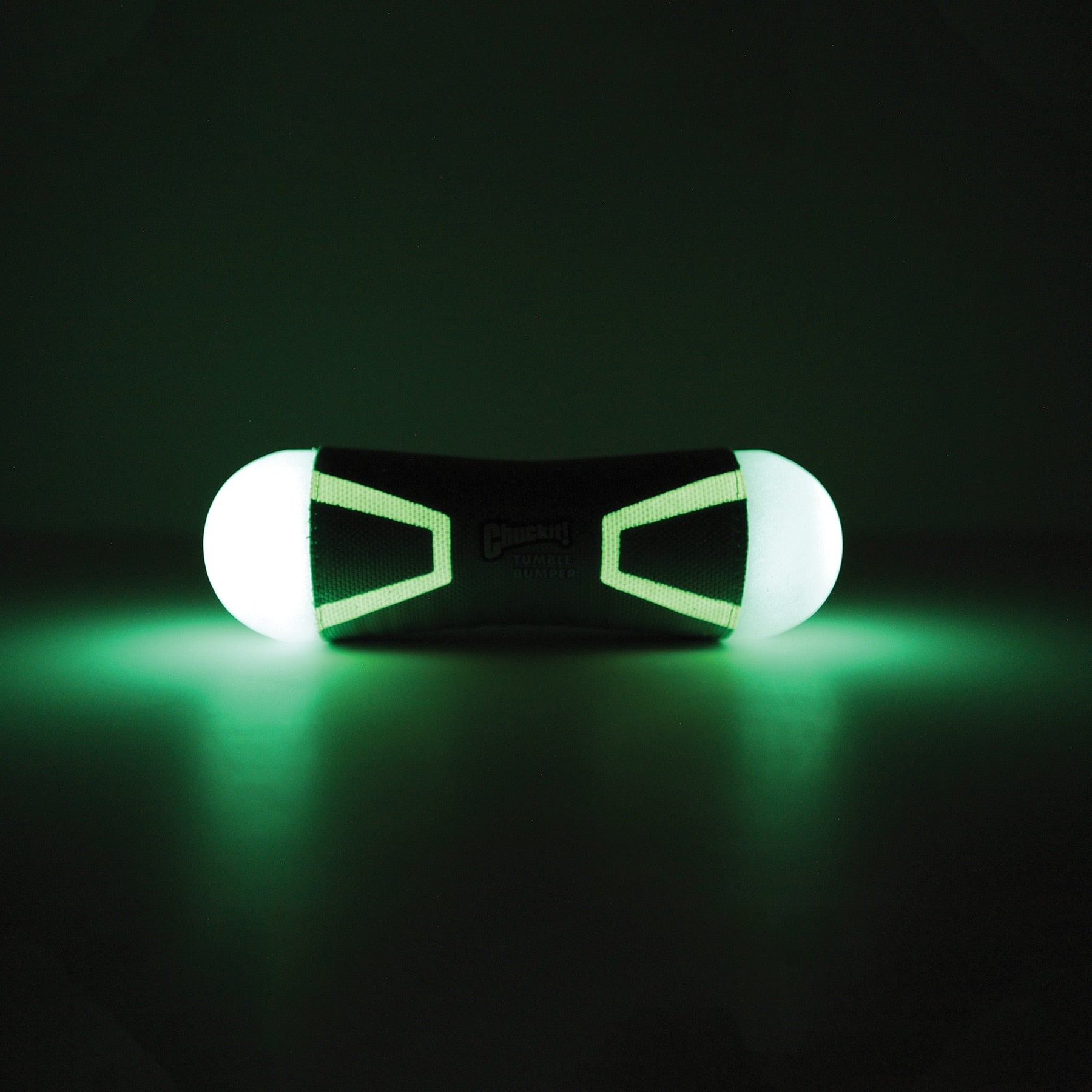The Chuckit! Tumble Bumper Max Glow by Chuckit illuminates two ends with a black core in a dark environment. Its cylindrical shape and glowing green light resemble a futuristic fetch toy from another world.