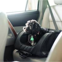 A small dog sits in a Gen7Pets Black Geometric Roller-Carrier on a light-colored cars backseat, peering out the window with a green-tagged collar.