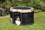 A dog with a black and brown coat and a white face sits inside an open Precision Pet Soft Side Play Yard on a grassy lawn, set against lush garden bushes and vibrant flowers. This water-resistant accessory is from Precision Pet Products.
