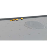 A gray PetFusion Pet Food Mat made from FDA-grade premium silicone with anti-slip bumps displays scattered yellow pills on the left and a puddle of clear liquid on the right.