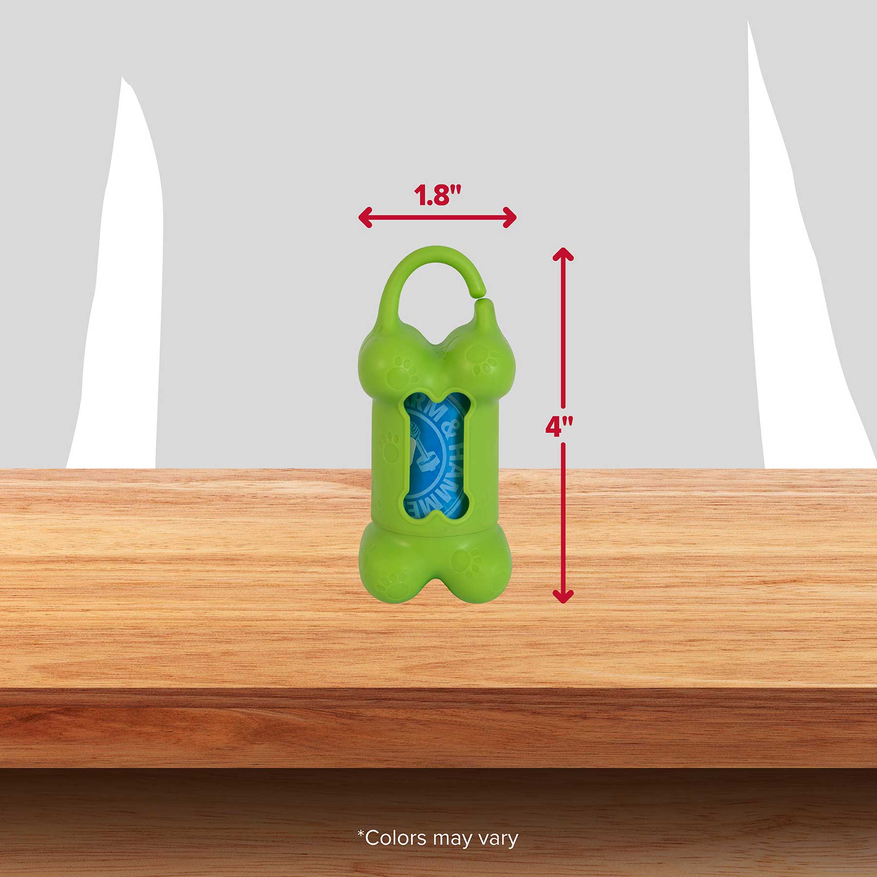 The Arm & Hammer Bone Dispenser & Disposable Waste Bag Set, designed in green and shaped like a bone, measures 1.8 wide by 4 tall with a blue bag roll that controls odors. It features a top clip and is displayed on wood against a gray backdrop. Note: Colors may vary.