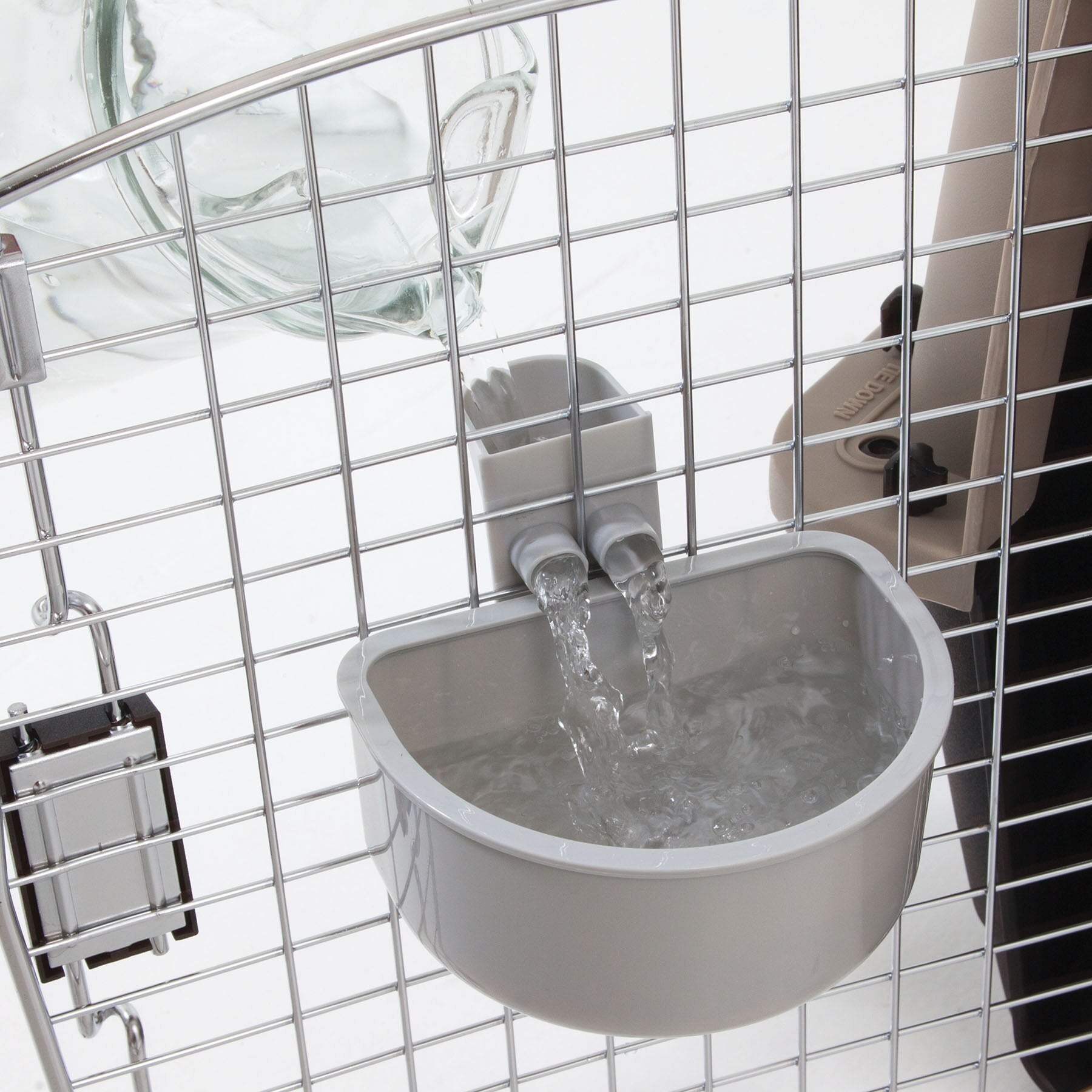 The Petmate No Spill Kennel Cup by Petmate is a gray automatic water dispenser attached to a metal cage, featuring a transparent bottle and dual spouts for spill-proof travel convenience.