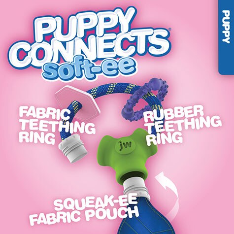 The JW Puppy Connects Soft-ee by JW, displayed on a pink backdrop, features a Puppy teething toy with a fabric teething ring, rubber ring, squeak-ee pouch, all linked by a cord for robust chewing fun.