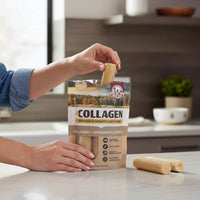 A person holds a Wild Eats Venison Flavor Collagen 5" Retriever Style Cheek Roll above an open 4-pack bag on a kitchen counter, with another collagen chew and kitchen items visible in the background.